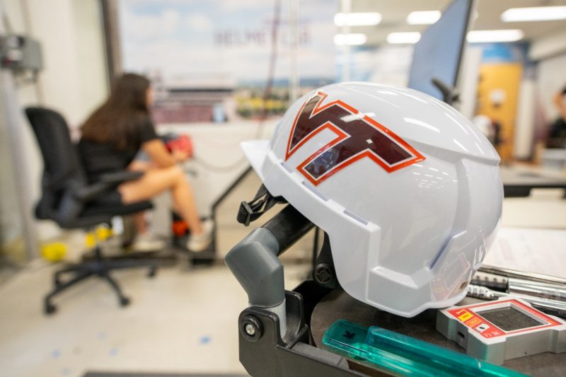 Helmet with Virginia Tech logo in the foreground. Student doing helmet research in the background. 