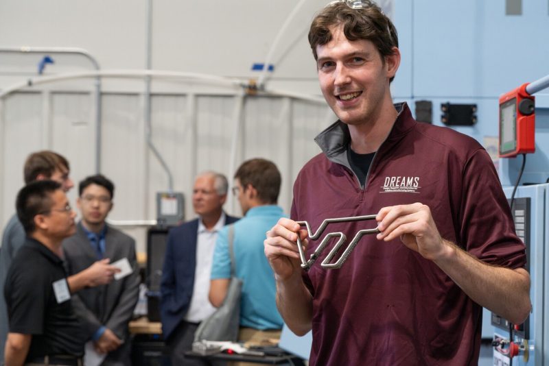 Man in a maroon pullover that says "DREAMS" on in holds up the 3D-printed logo of Virginia Tech.