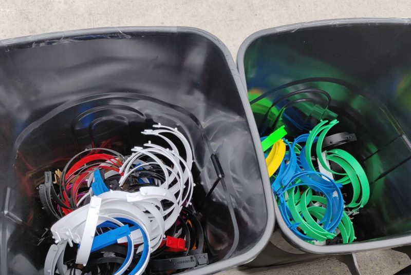 Dozens of 3-d printed headbands in two gray bins. The headbands range in color including white, blue, red, yellow, green, and black.